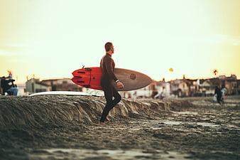 Surfer walking on beach at sunset with red surfboard