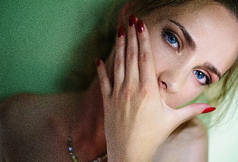 Close-up of woman with blue eyes and red nails covering mouth