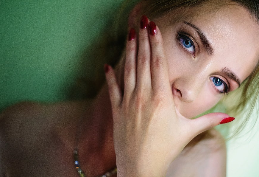 Close-up of woman with blue eyes and red nails covering mouth