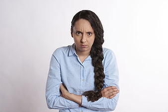 Frustrated young woman with crossed arms and scowl on white background