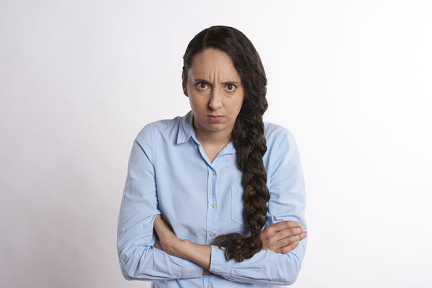 Frustrated young woman with crossed arms and scowl on white background