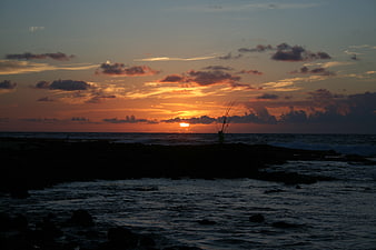 Silhouette of Fisherman on Rocky Coast at Sunset