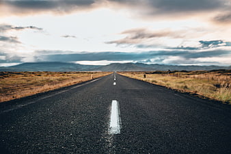 Straight asphalt road leading to distant mountains under cloudy sky