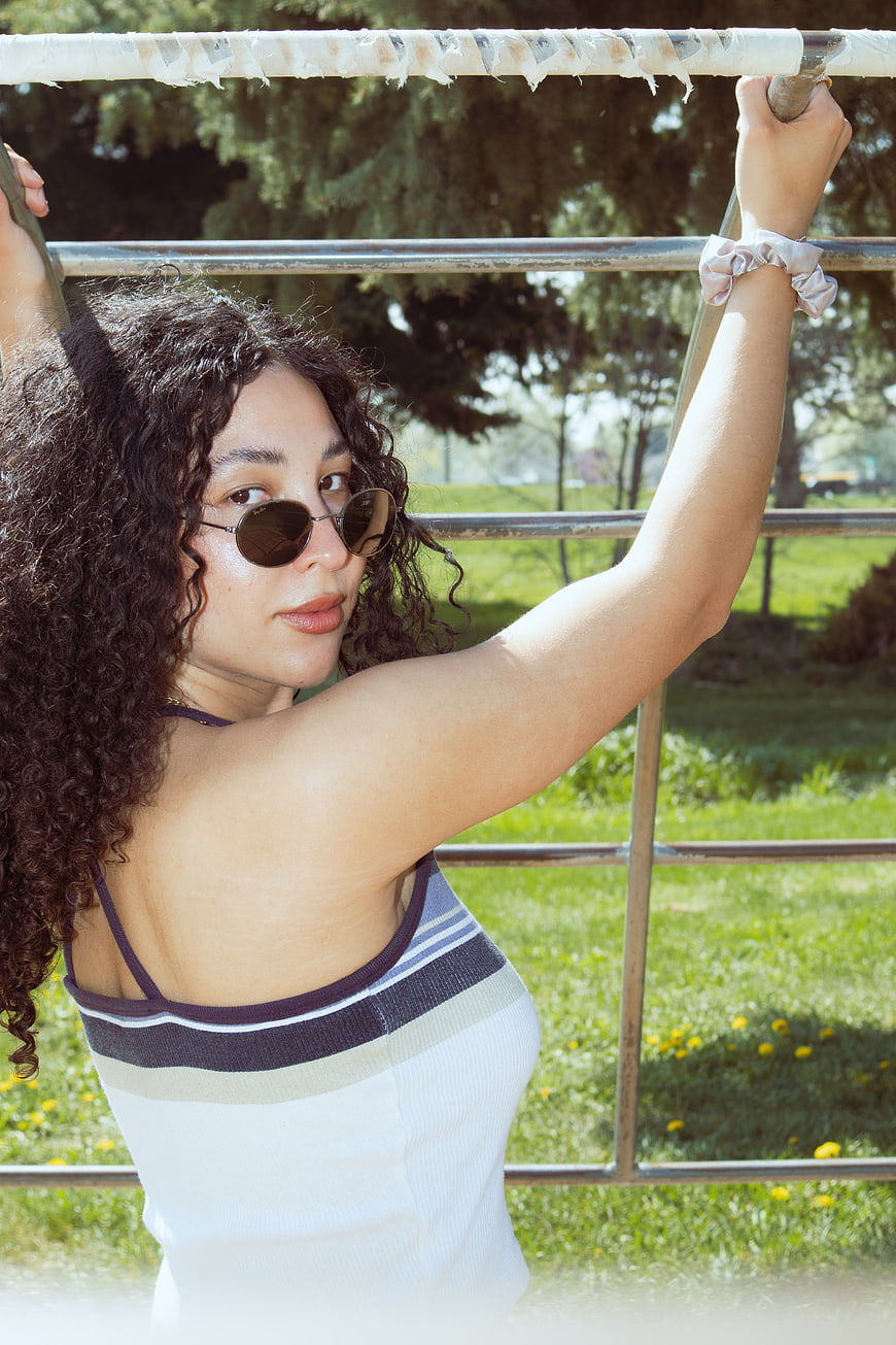 Young woman with curly hair and sunglasses hanging on monkey bars