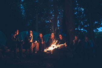 Group of friends sitting around a campfire in the forest at night