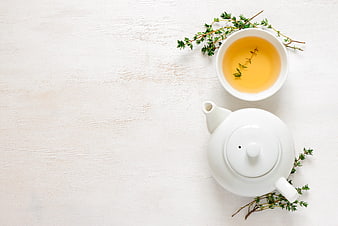 White teapot and cup of herbal tea with thyme sprigs on white background