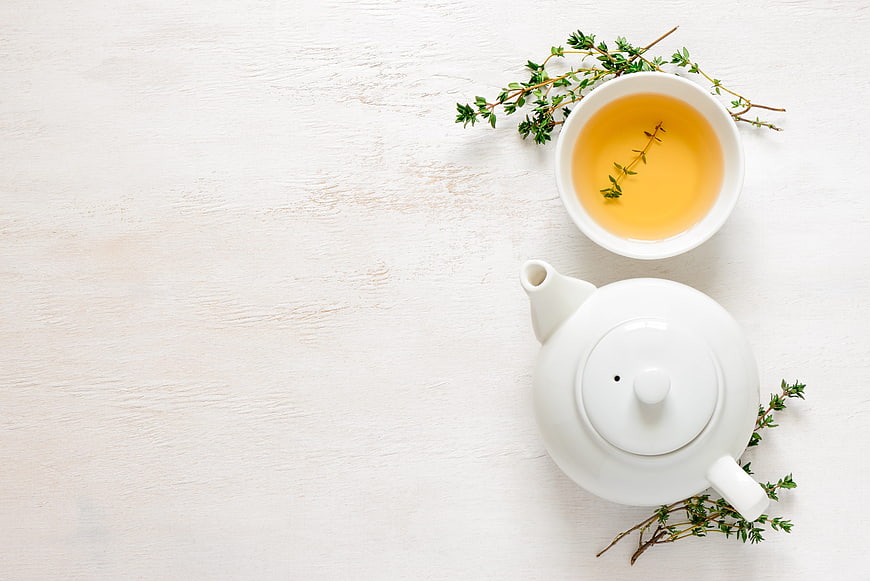 White teapot and cup of herbal tea with thyme sprigs on white background