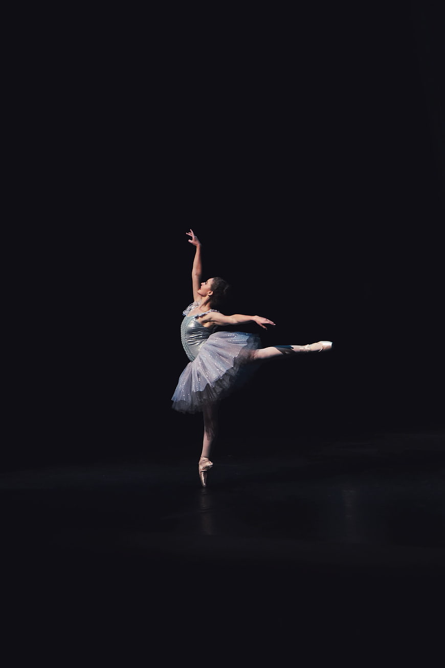 Ballerina performing arabesque pose on dark stage