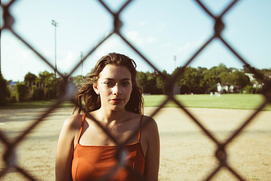 Young woman portrait through chain link fence in park