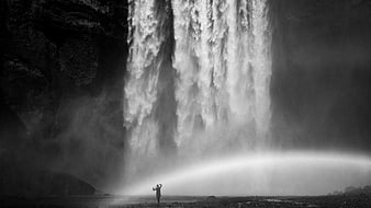 Silhouette of person standing before massive waterfall in black and white