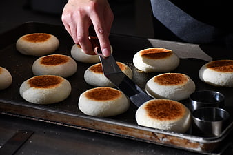 Baker cutting freshly baked bread rolls on a tray