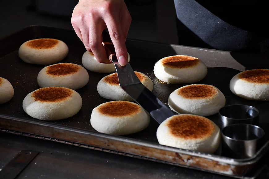 Baker cutting freshly baked bread rolls on a tray