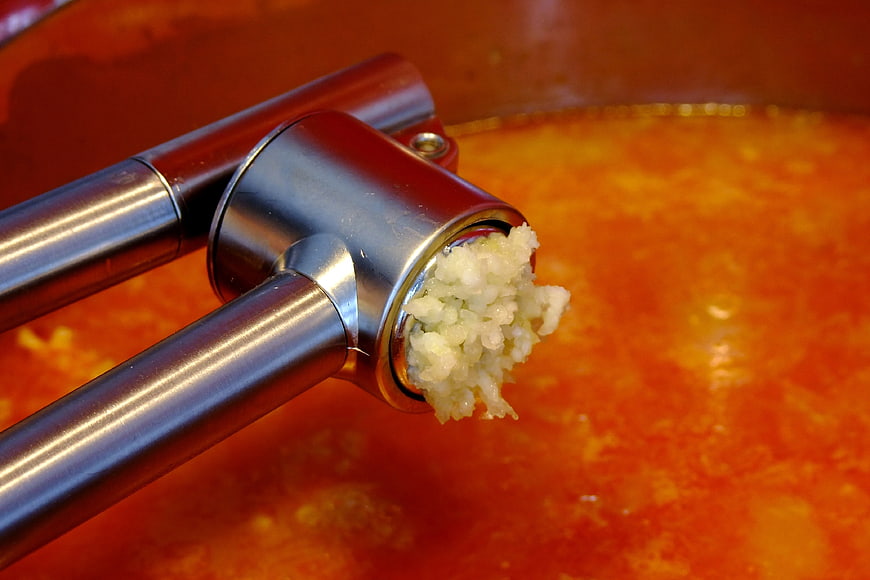 Garlic Press Squeezing Minced Garlic Over Red Sauce