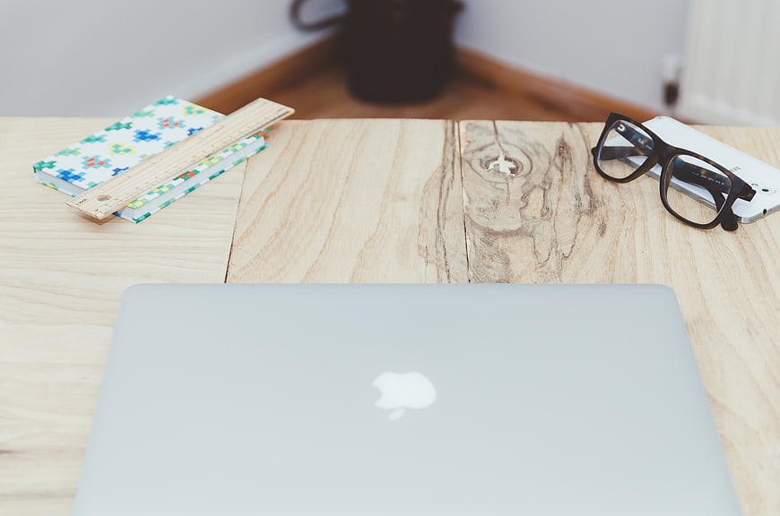 Minimalist wooden desk with laptop, glasses, and notebook