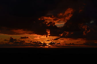 Dramatic fiery sunset with dark clouds over ocean horizon