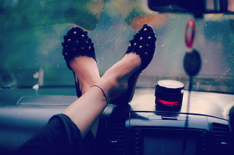 Woman's legs in black heels resting on car dashboard