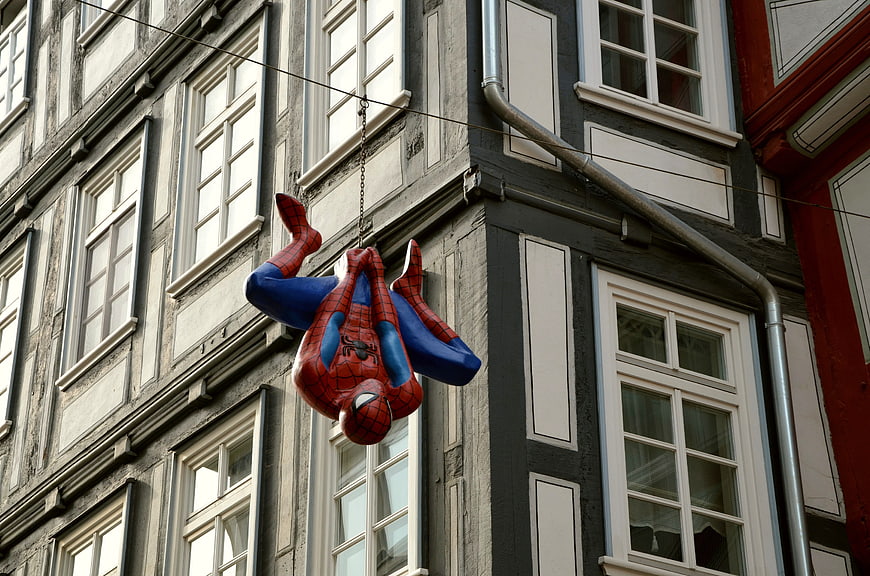Spiderman statue hanging upside down on historic building facade