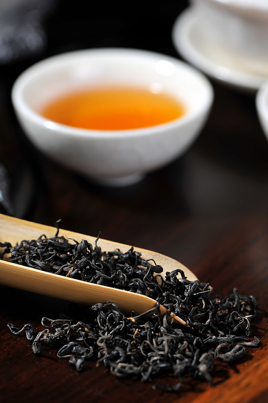 Loose black tea leaves in bamboo scoop with amber tea cup