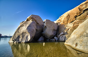 Large granite boulders in clear blue water under sunny sky