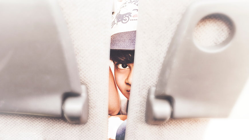 Child peeking through car seat gap with magazine