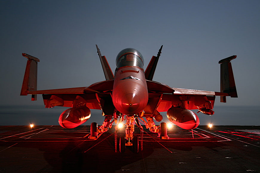 Front view of F-18 Super Hornet fighter jet on aircraft carrier deck at dusk