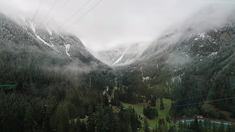 Misty Alpine Valley with Snow-Capped Peaks and Forest