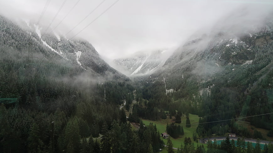 Misty Alpine Valley with Snow-Capped Peaks and Forest