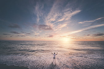 Man with arms raised in ocean waves at sunset