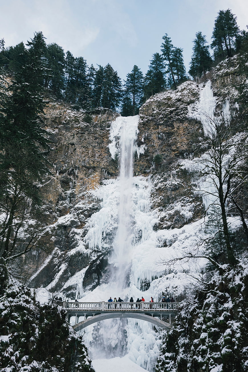 Frozen waterfall with bridge and tourists in winter forest
