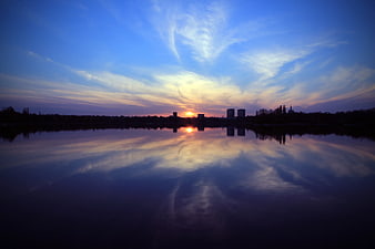 Serene Sunset Reflection Over Calm Lake and City Skyline