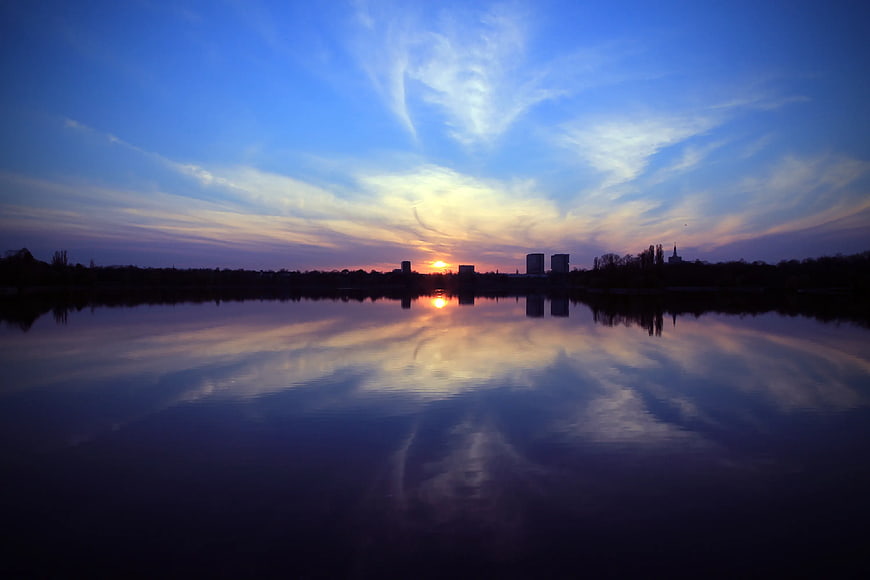 Serene Sunset Reflection Over Calm Lake and City Skyline