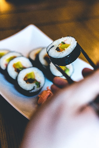 Close-up of hand holding sushi roll with chopsticks