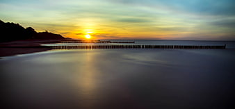 Serene Sunset Over Calm Beach With Wooden Breakwater