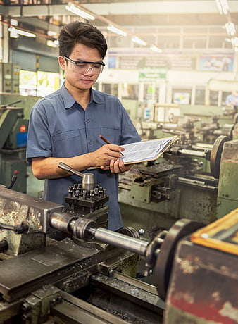 Asian male factory worker inspecting machinery with clipboard