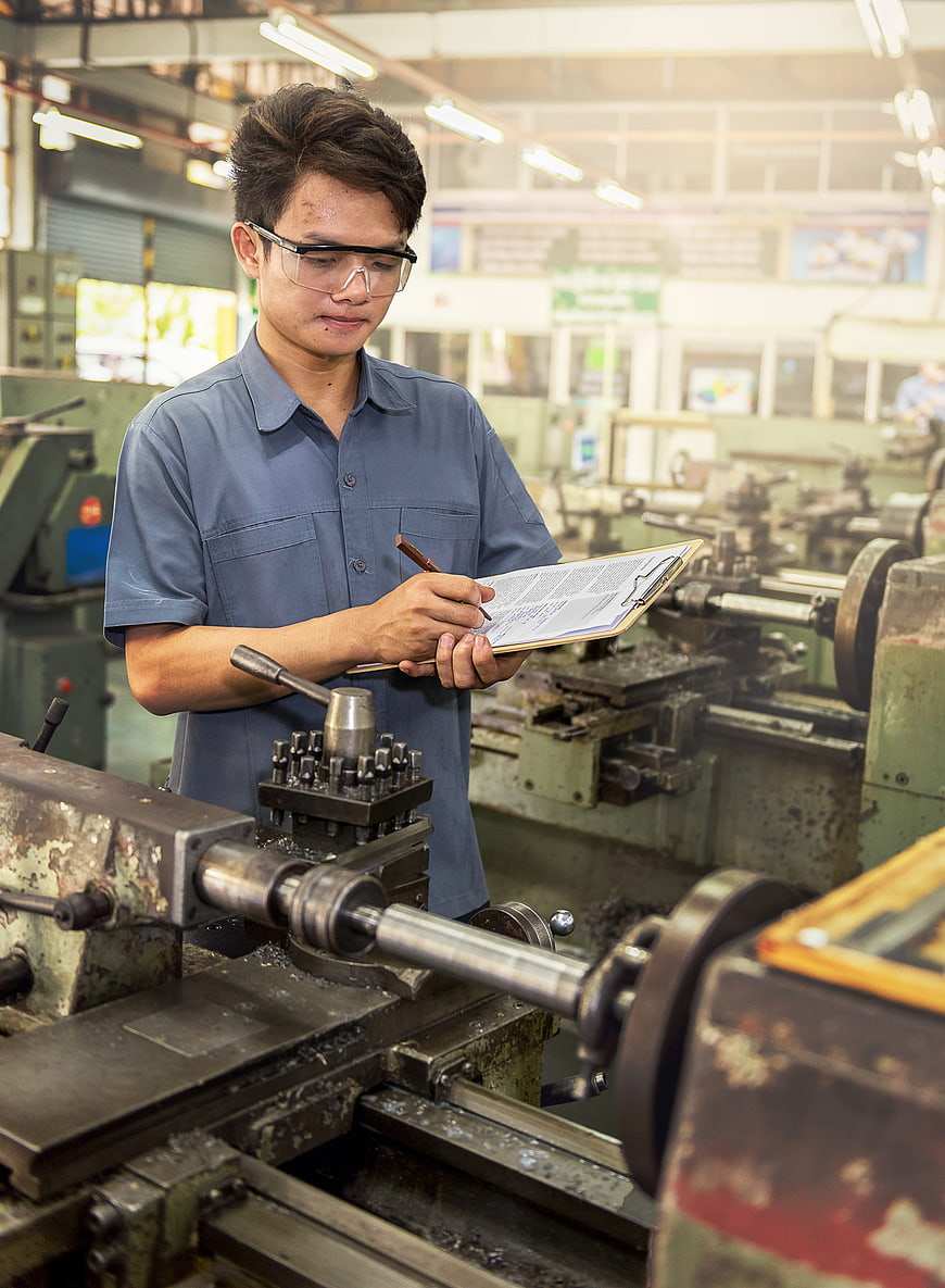 Asian male factory worker inspecting machinery with clipboard