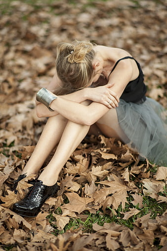 Sad woman sitting in autumn leaves wearing ballet tutu