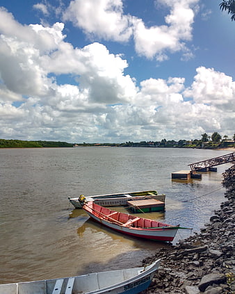 Colorful boats moored on a wide river under a cloudy blue sky