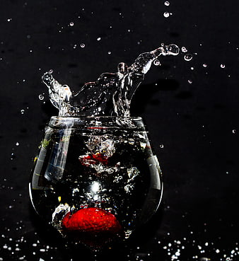 Strawberry splashing into water in a glass on black background