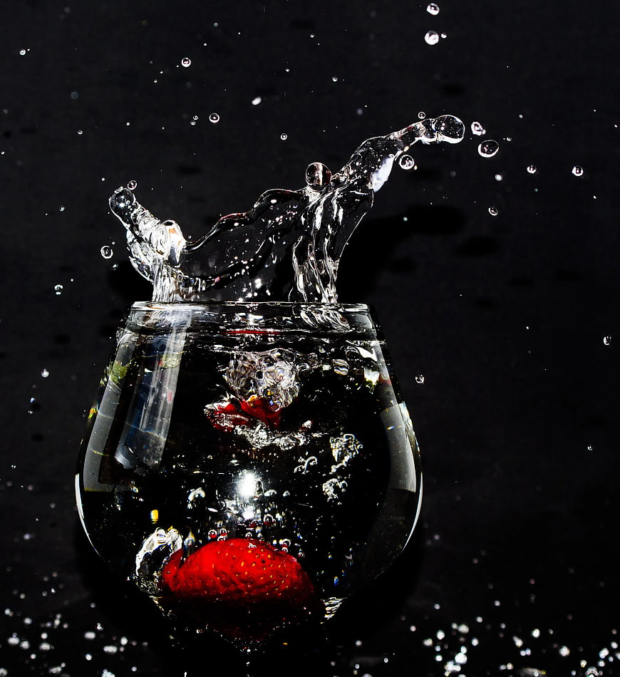 Strawberry splashing into water in a glass on black background