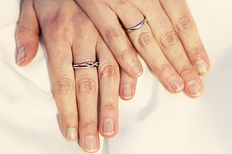 Close-up of two hands with wedding rings on white fabric