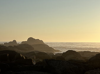 Golden sunset over rocky ocean coastline with silhouetted boulders