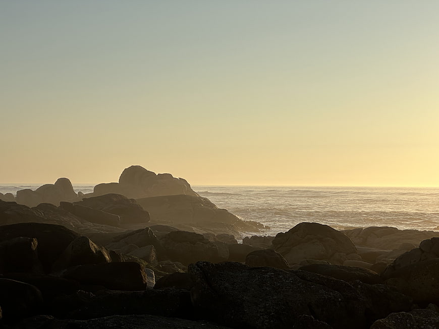 Golden sunset over rocky ocean coastline with silhouetted boulders