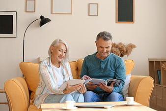 Happy senior couple reading magazines on yellow sofa