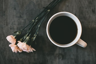 Top View of Black Coffee Cup and Pink Carnations on Dark Wood