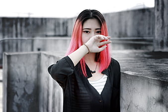 Young Asian woman with pink hair posing on a concrete rooftop