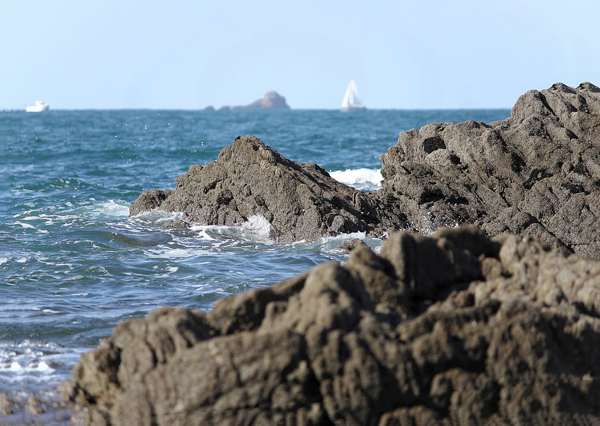 Rugged coastal rocks with ocean waves and distant sailboat