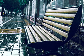 Empty wooden bench on wet sidewalk during rainy day