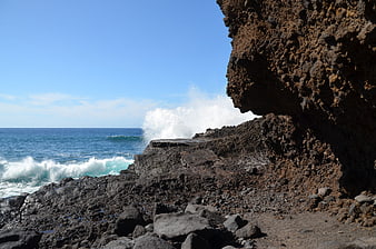 Ocean waves crashing against rugged volcanic rock coastline