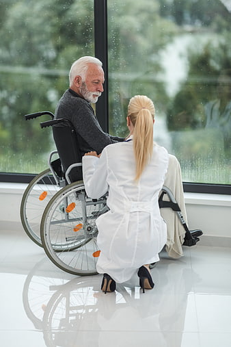 Doctor comforting elderly man in wheelchair by window
