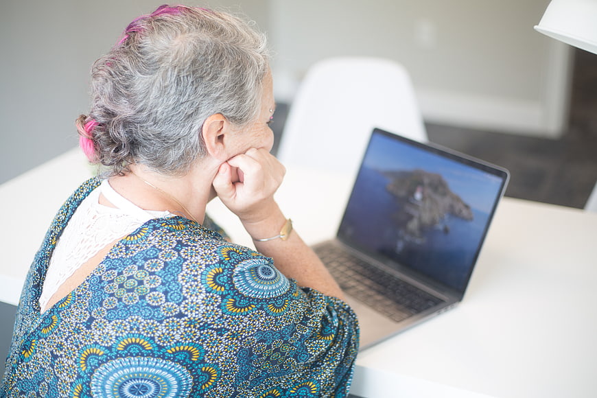 Senior woman with pink hair using laptop at home
